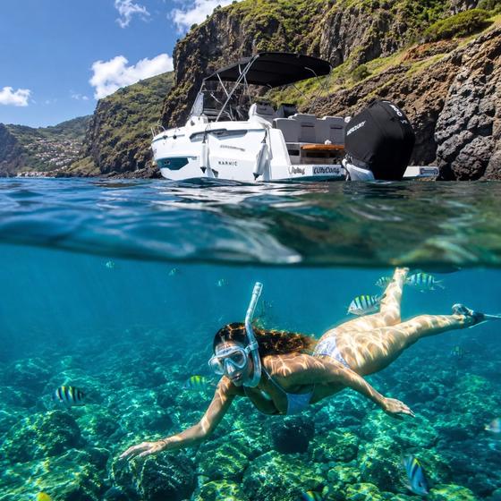 A guest snorkelling in a clear cove below the Madeira cliffs, seen half above and half below the water