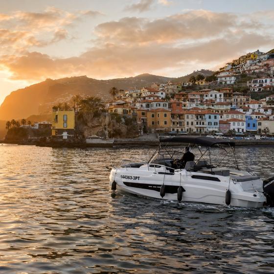 The painted houses of Câmara de Lobos seen from the water at golden hour